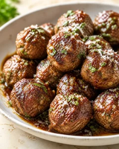 bowl of browned meatballs in glossy brown glaze, topped with parsley and parmesan