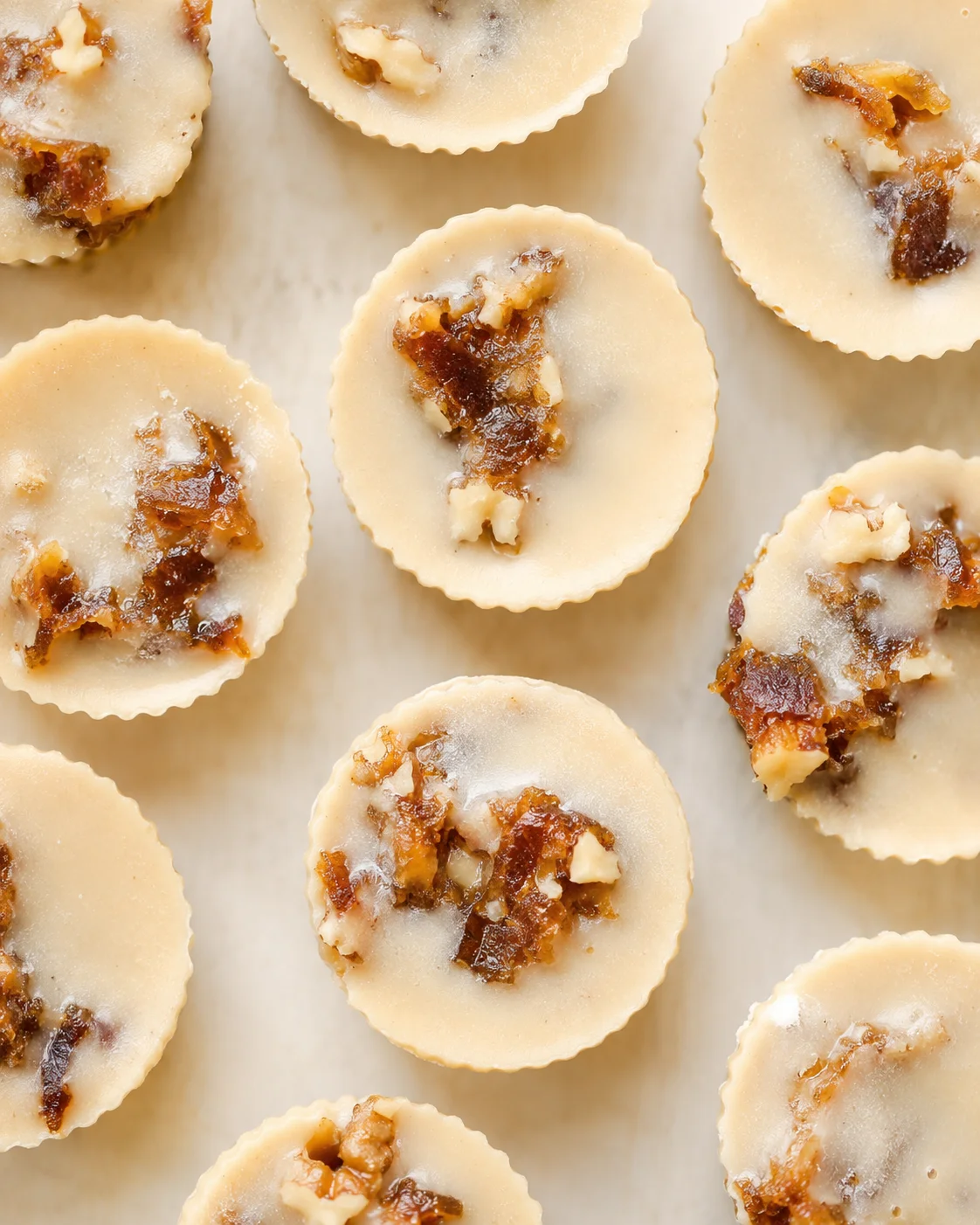 Small round mini tarts with pale crust and nut-topped centers on parchment.