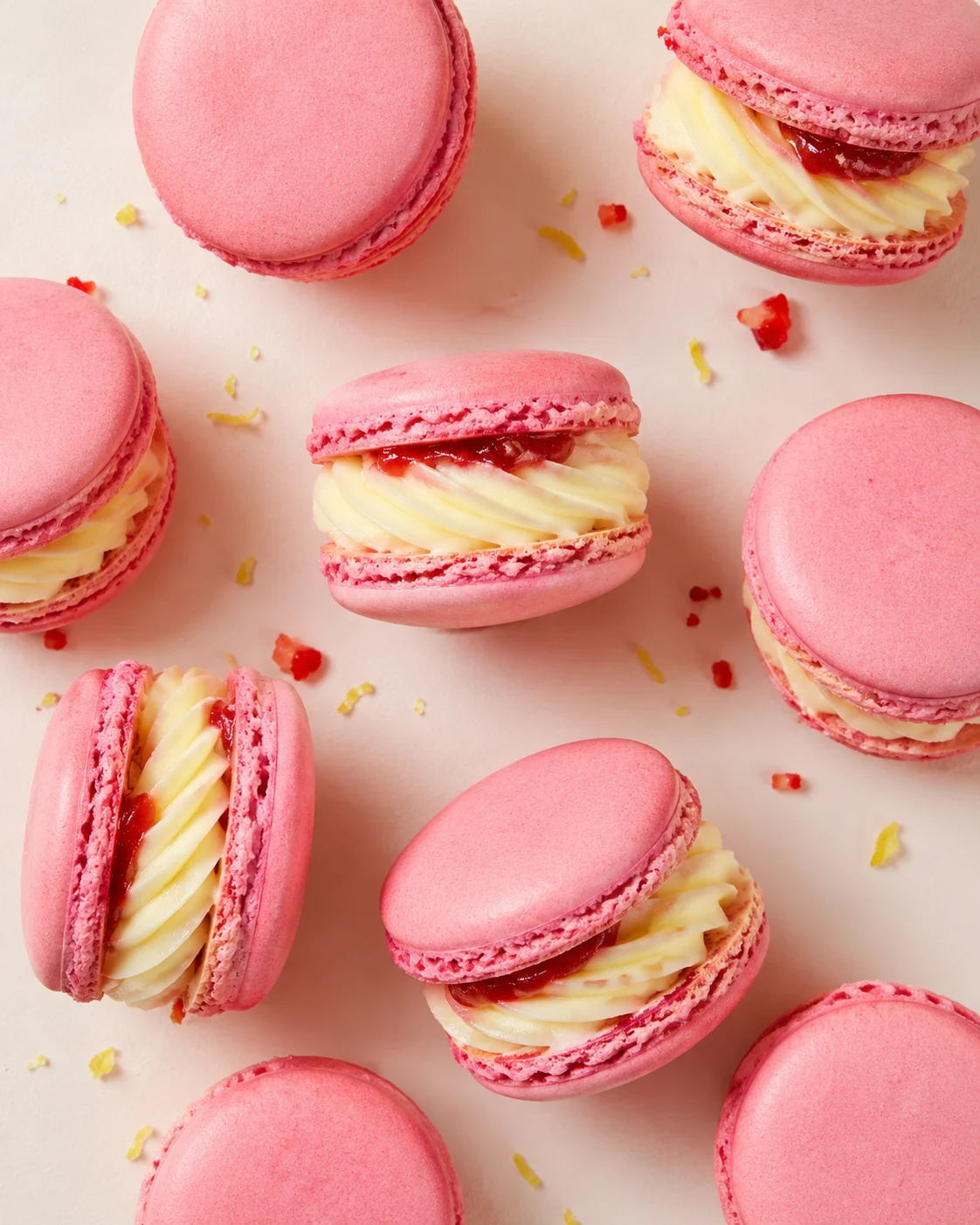 Several pink macarons with white piped cream and jam centers on a pale pink background.