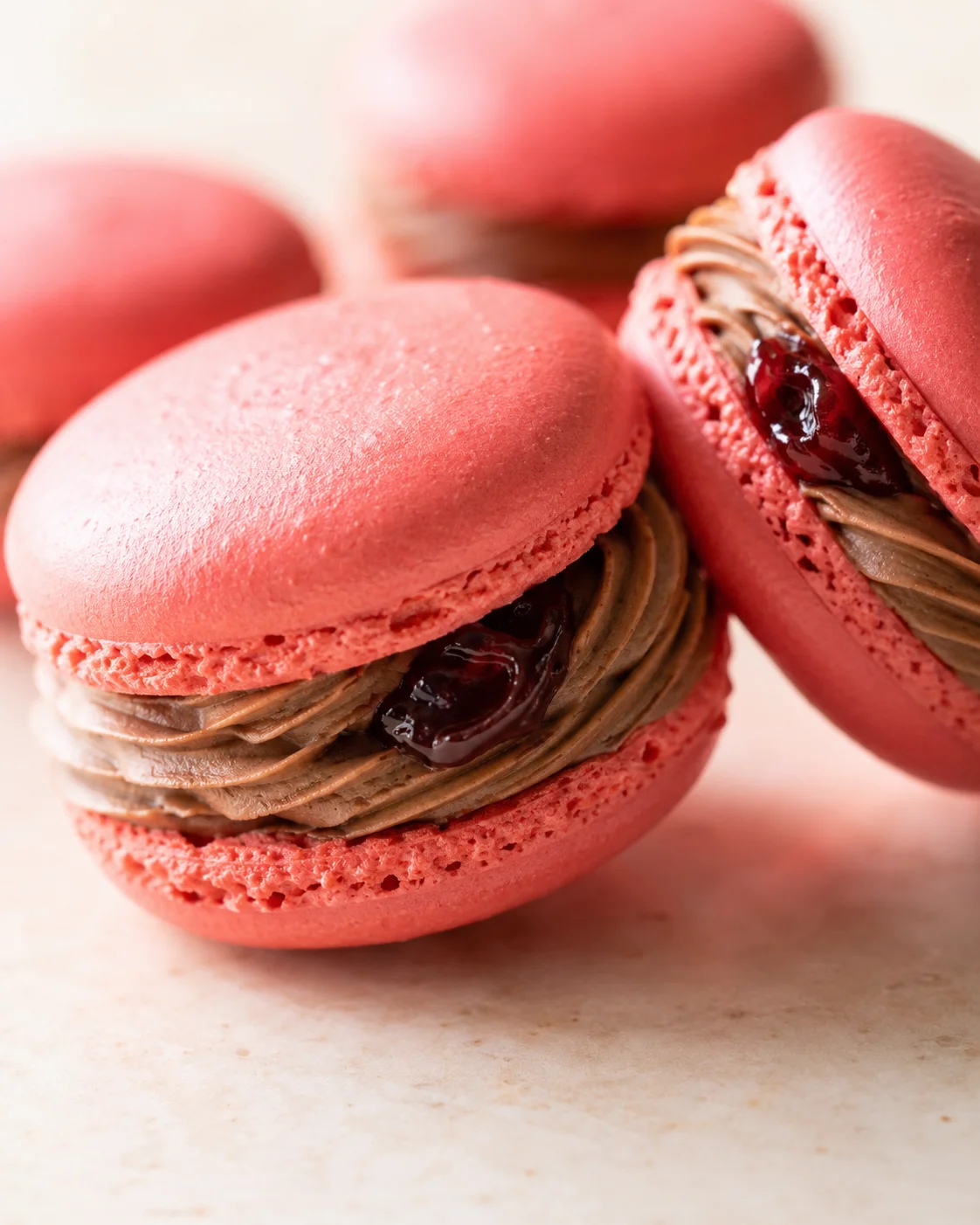 Close-up of pink macarons with chocolate ganache and cherry jam filling on a pale countertop
