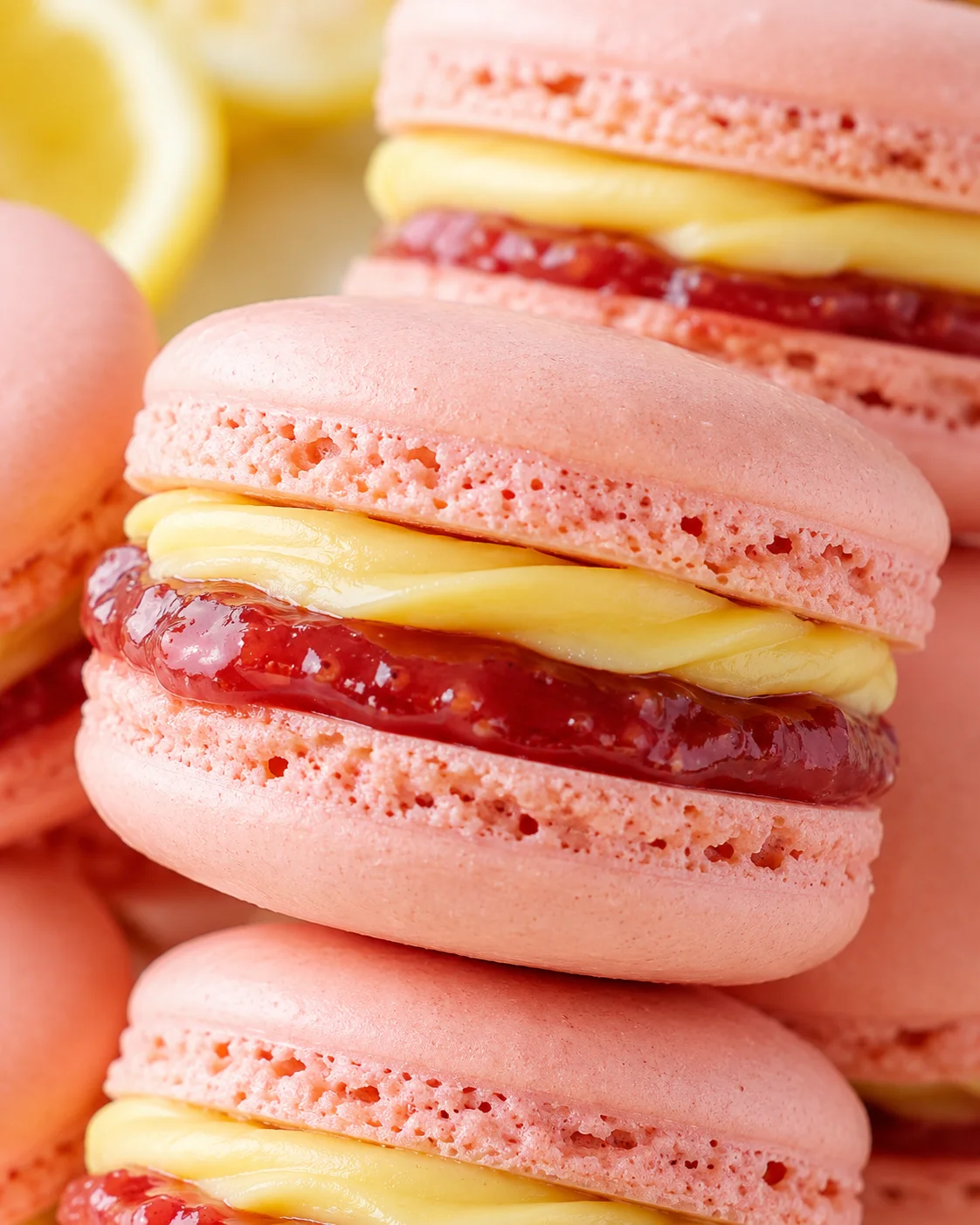 Close-up of pink macarons stacked with lemon-yellow cream and red jam filling.