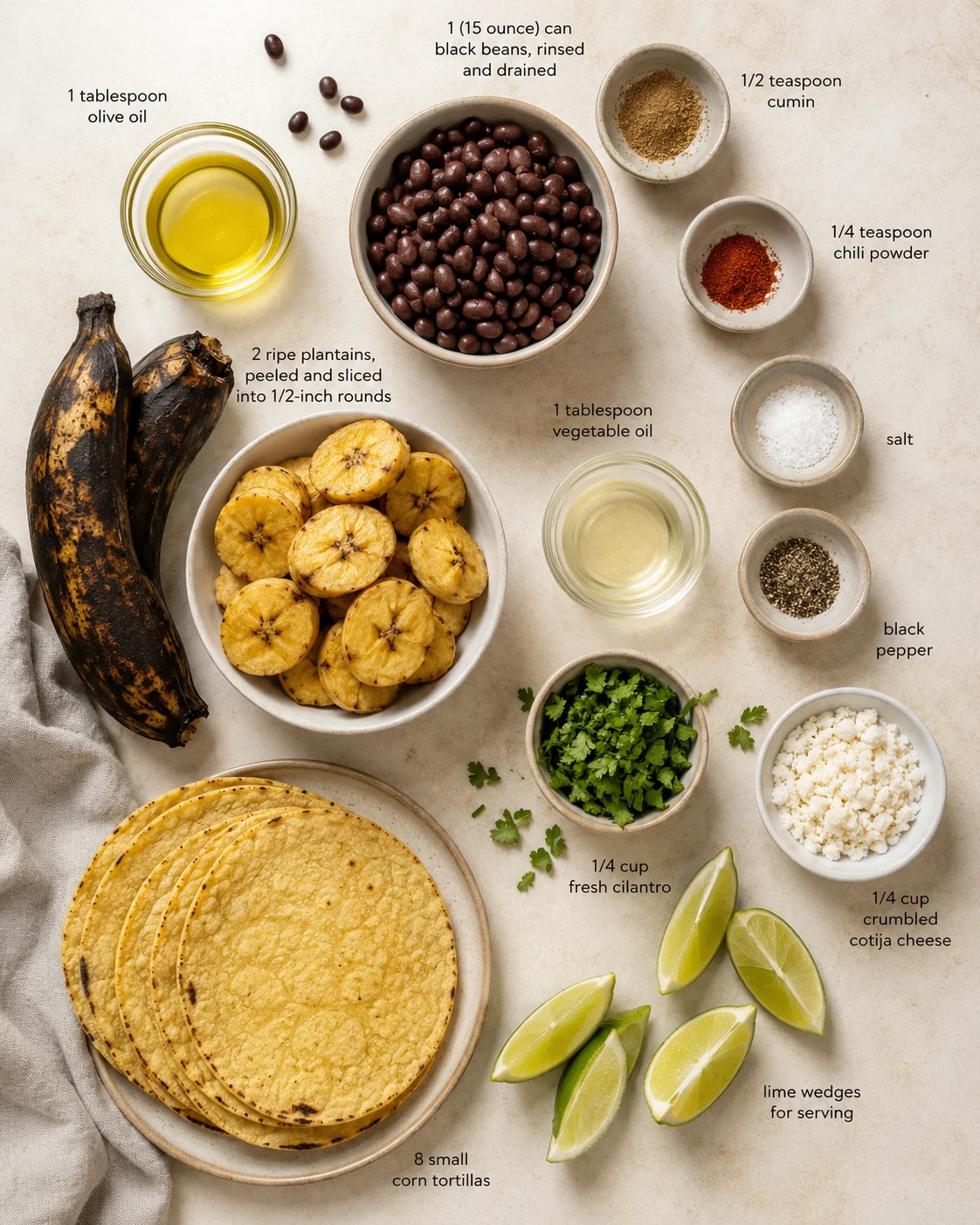 Overhead view of plantains, black beans, tortillas, cilantro, lime wedges and spices laid out.