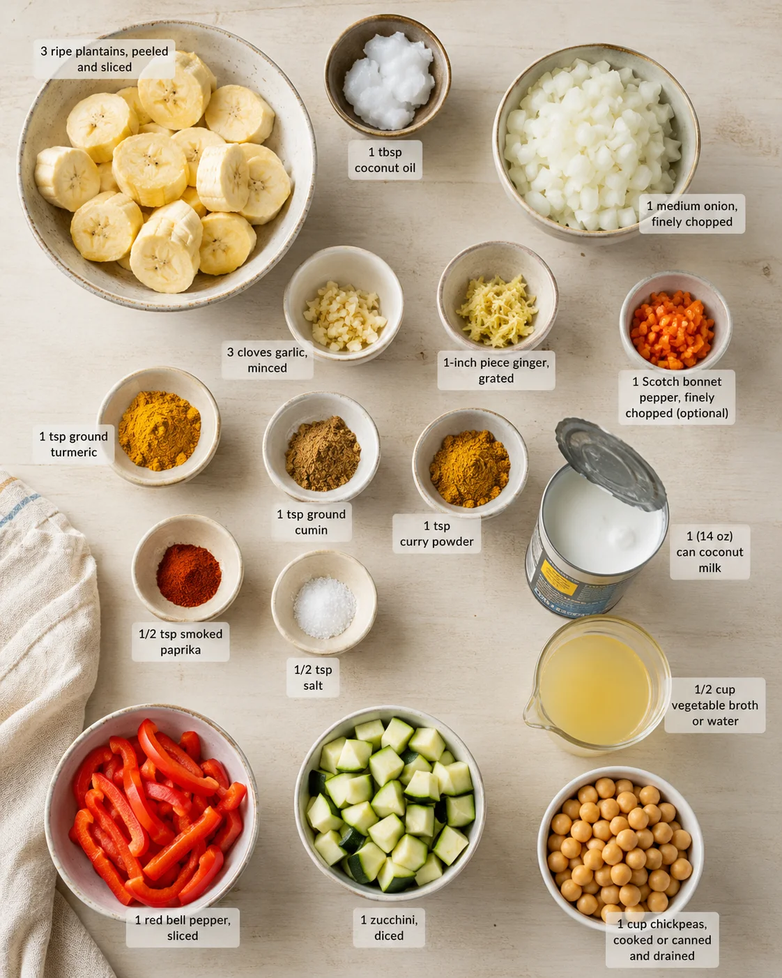 Top-down view of a kitchen countertop with bowls of plantains, onions, coconut milk, chickpeas, peppers, and spices labeled for curry.