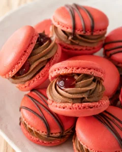 Close-up of bright red macarons filled with chocolate cream and a chocolate drizzle on a plate