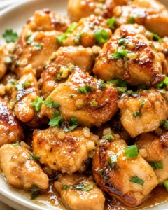 close-up of golden-brown chicken pieces in glossy sticky sauce, topped with green onions and cilantro.