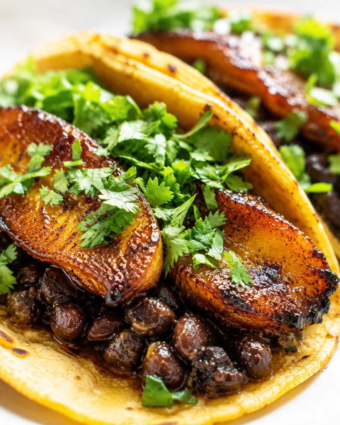 close-up of a finished taco with caramelized pork, beans, plantain, and cilantro