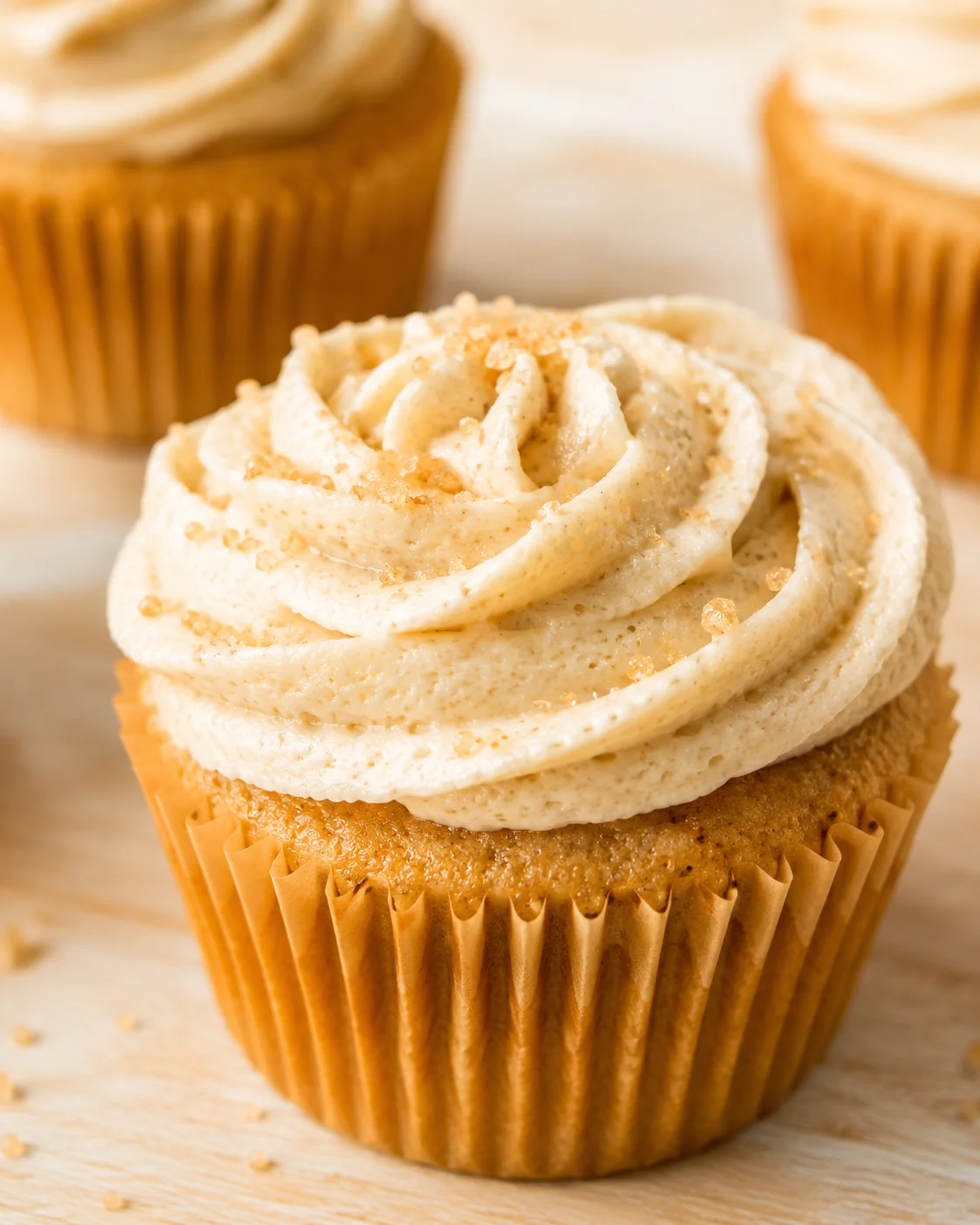 Close-up of a cupcake with swirled vanilla buttercream, sugar crystals, on a wooden table.