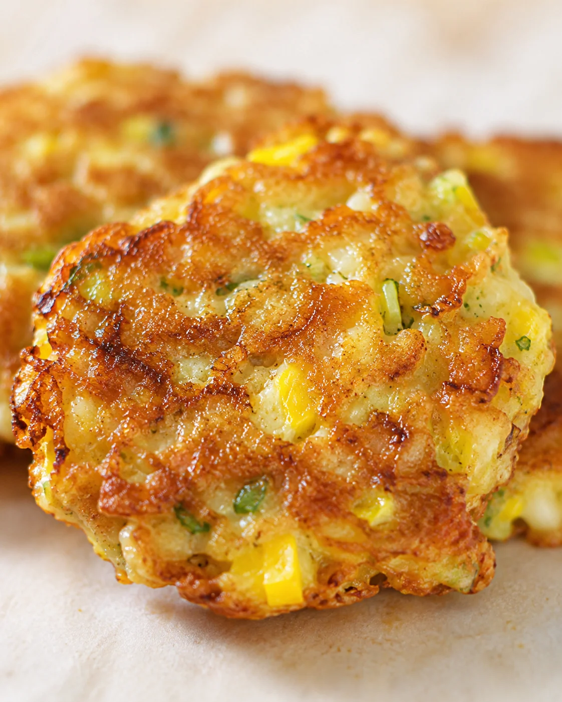 close-up of golden-brown corn and potato fritters with green onions on parchment.