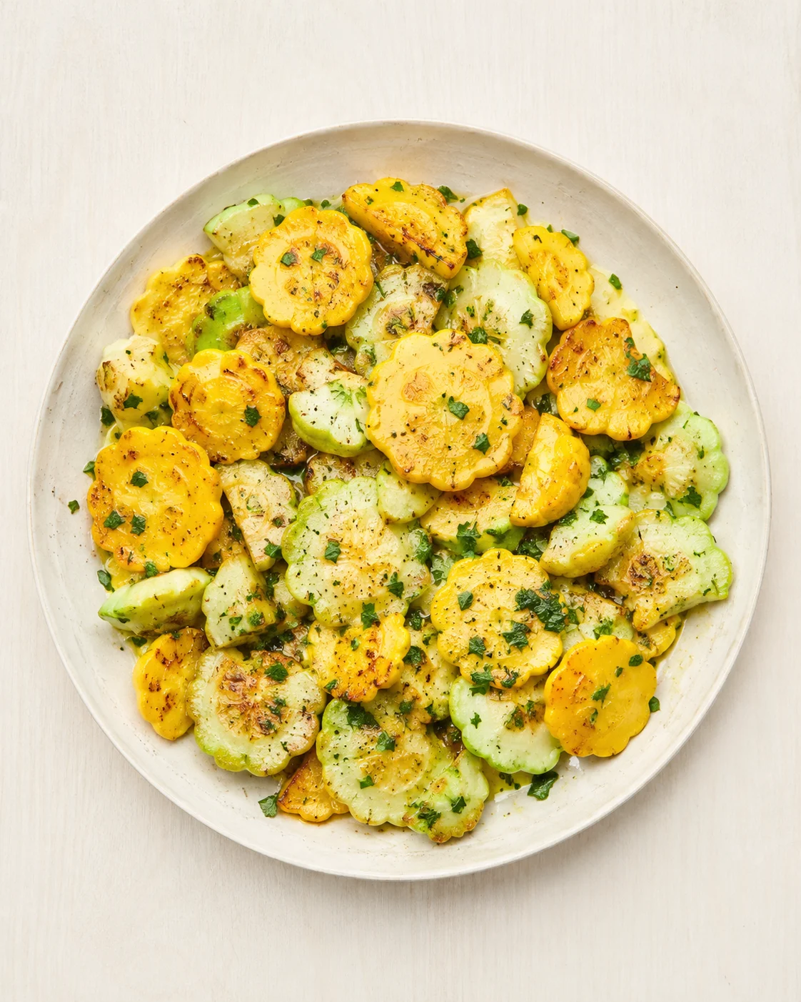 Beige plate of roasted yellow and green pattypan squash slices garnished with chopped herbs.