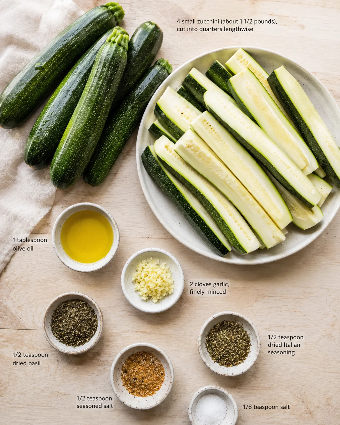 Top-down view of whole and cut zucchini with bowls of olive oil, garlic, and spices.